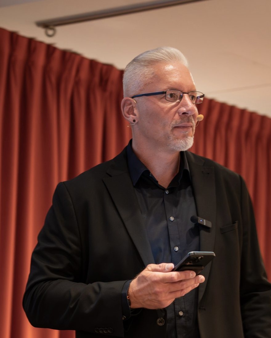 Reiner Küstner steht ruhig auf der Bühne, das Handy in der Hand