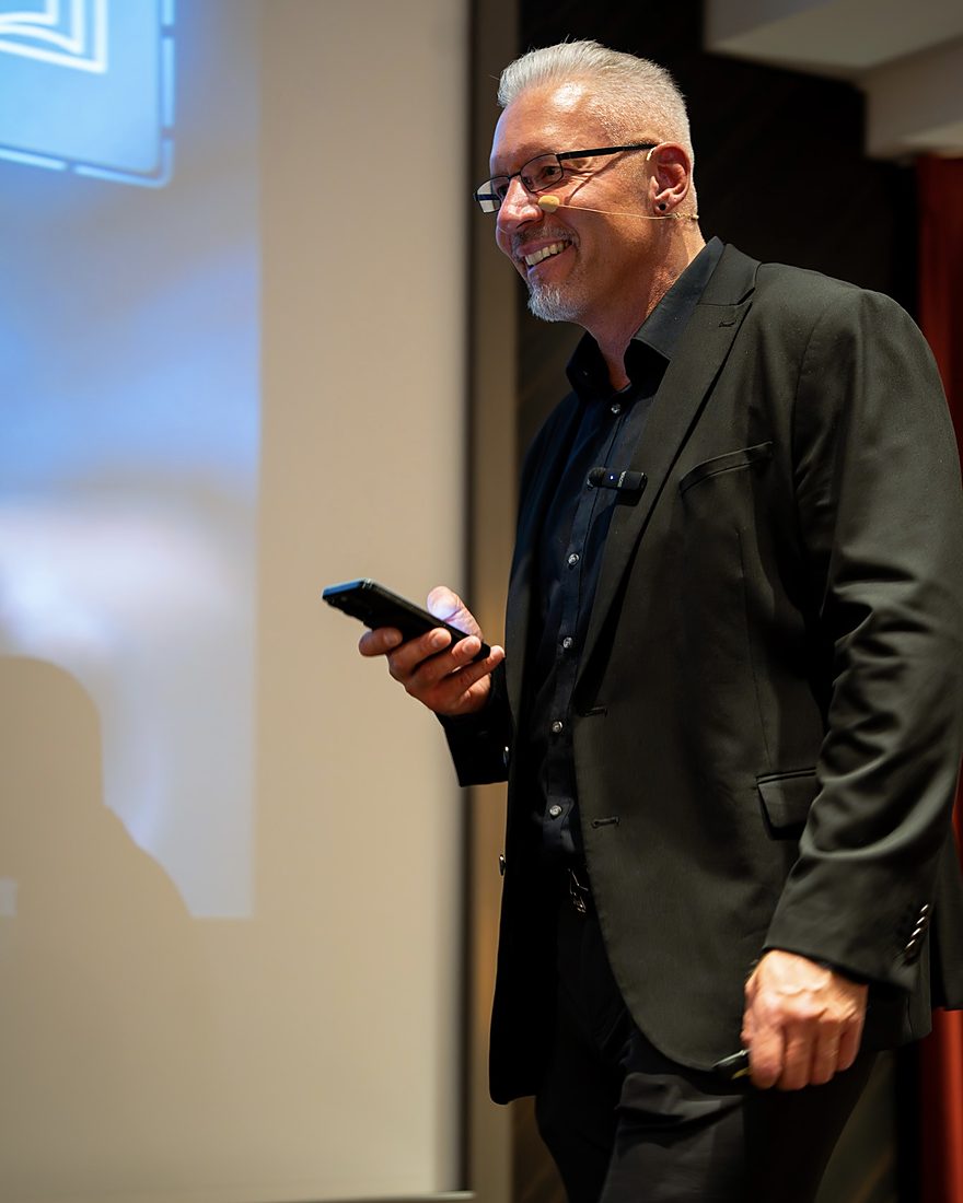 Reiner Küstner lächelt im Seminar, mit dem Handy in der Hand